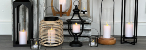 A collection of candles and lanterns arranged on a rustic wooden floor, creating a warm and inviting atmosphere.